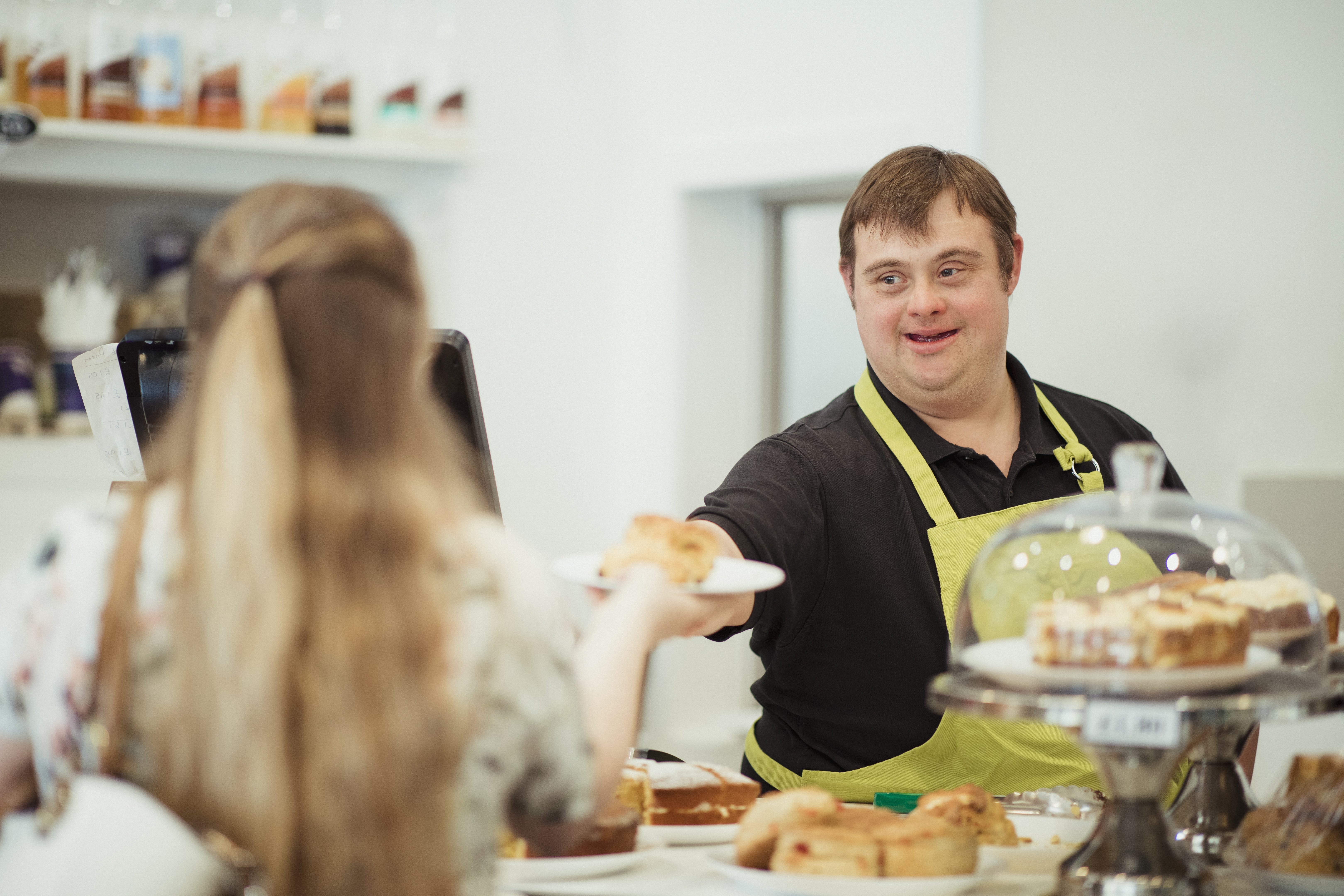 Ein Mann mit Down-Syndrom serviert einer Frau in einem Café, in dem er arbeitet, ein Brötchen.