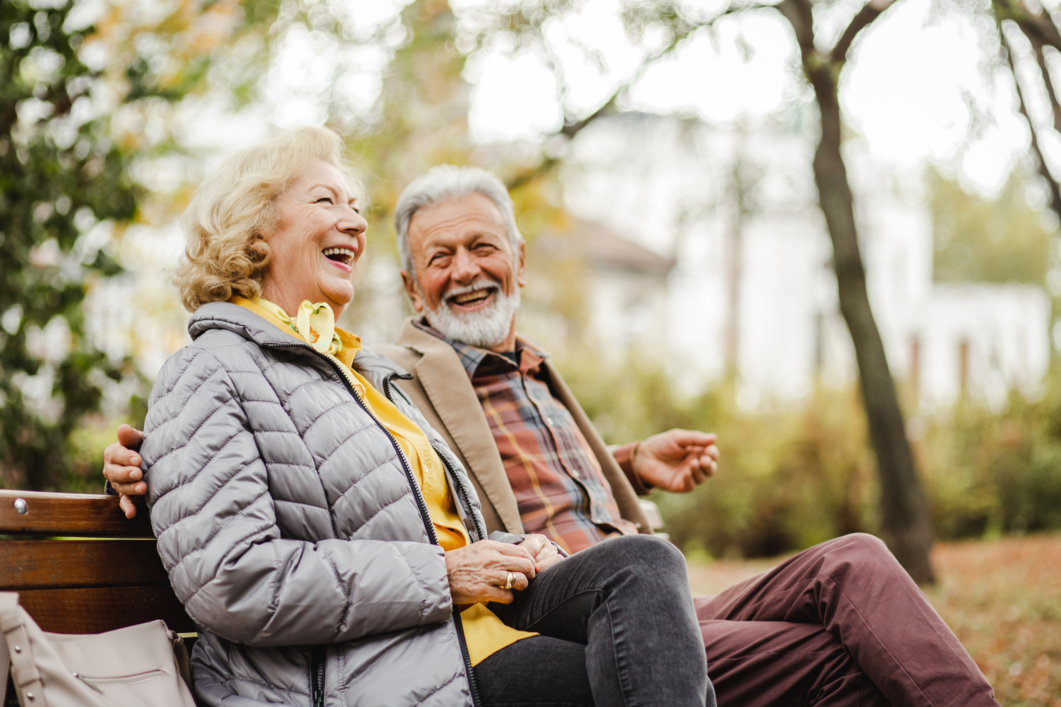 Glückliches Senior-Paar sitzt lachend auf der Bank im Park